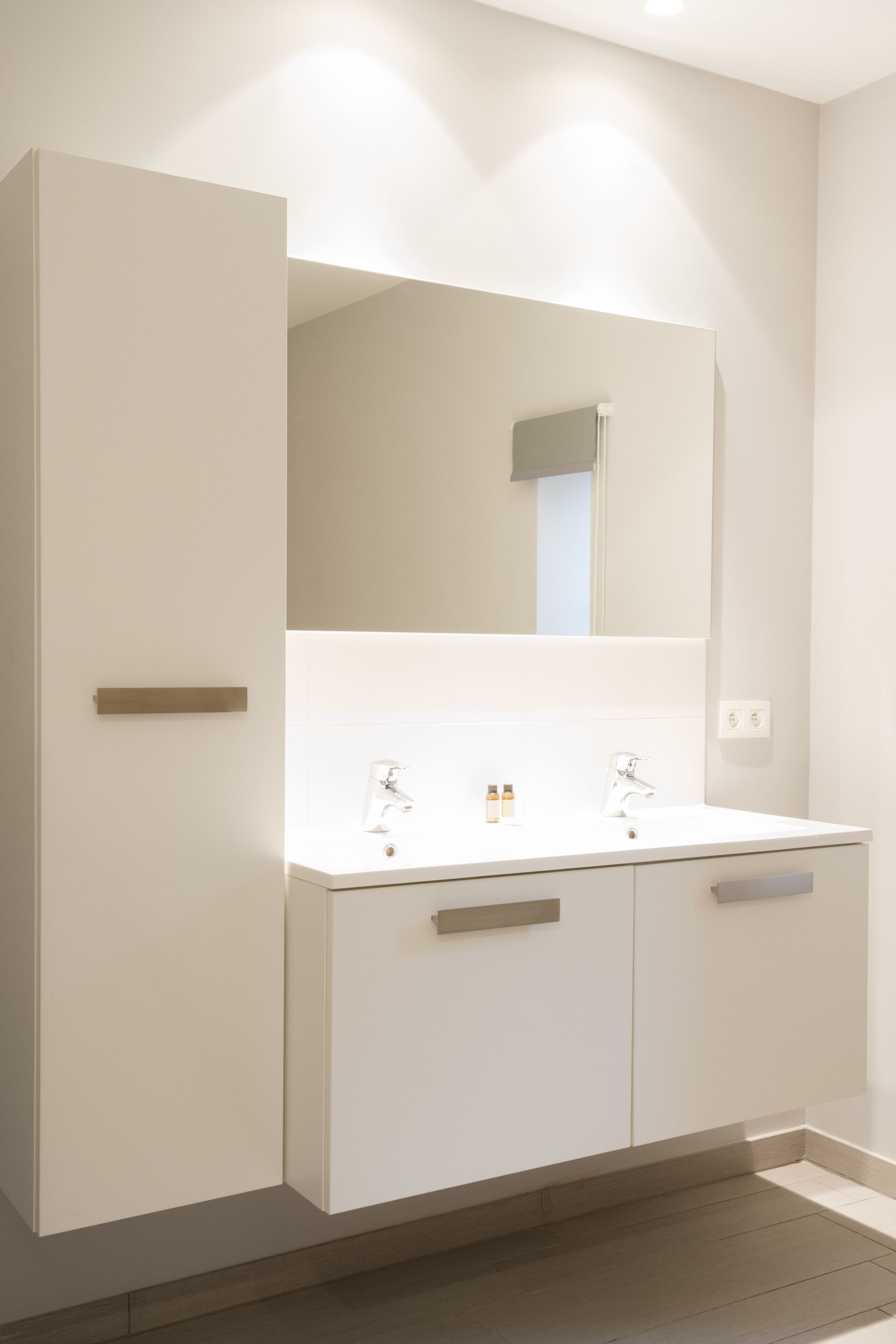 Ein modernes Badezimmer mit einem weißen Waschtisch, zwei Waschbecken und einem großen Spiegel.