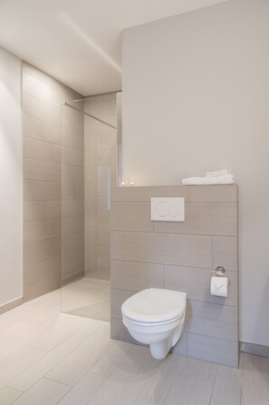 A modern bathroom with a toilet, a glass shower enclosure, and a towel rack. - Loweide (Oostkamp)