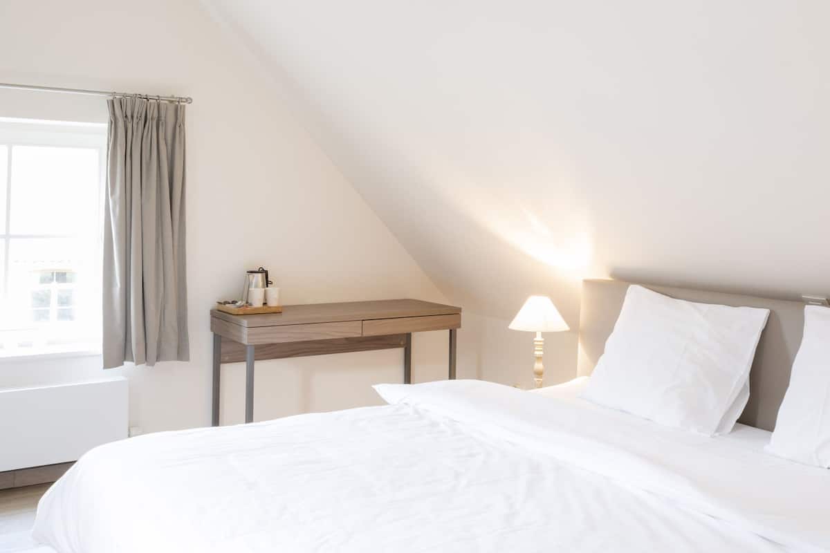 A bedroom with a bed, a bedside table, a lamp, and a hanging light fixture.
