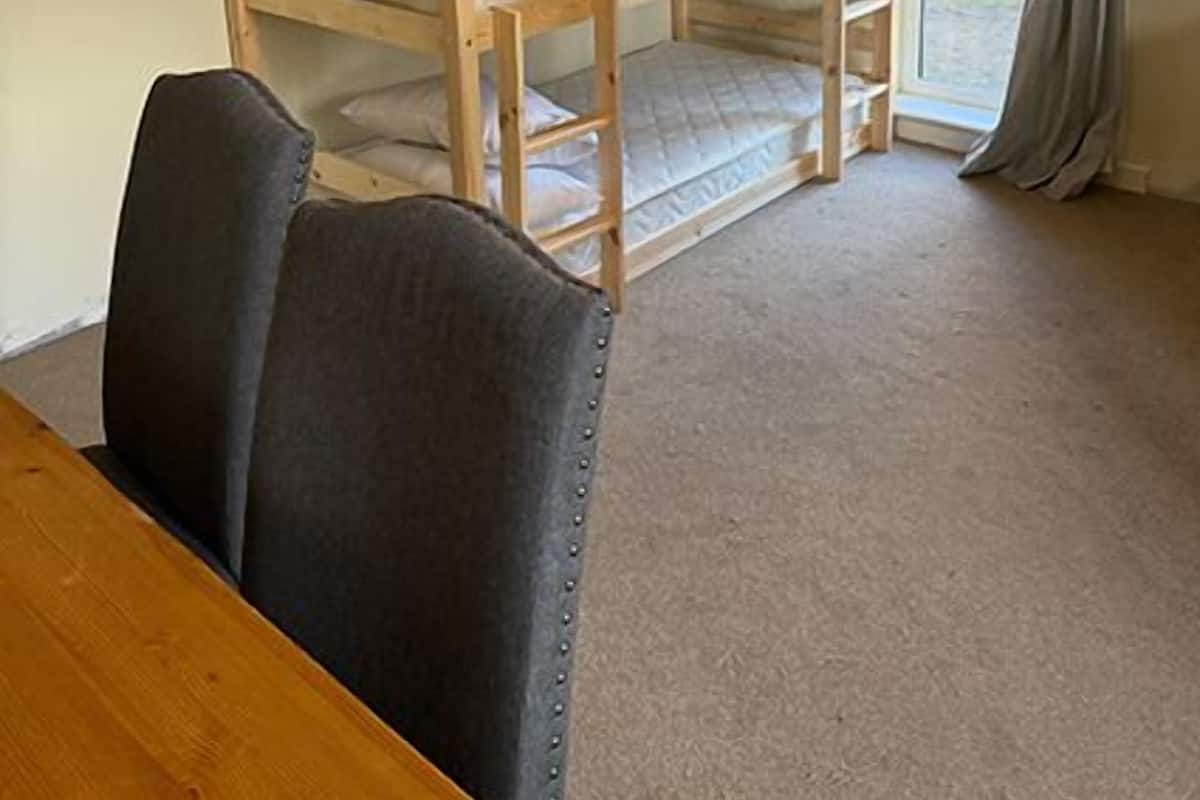 A bunk bed room with a wooden table and chairs, carpeted floor, and a window with curtains.