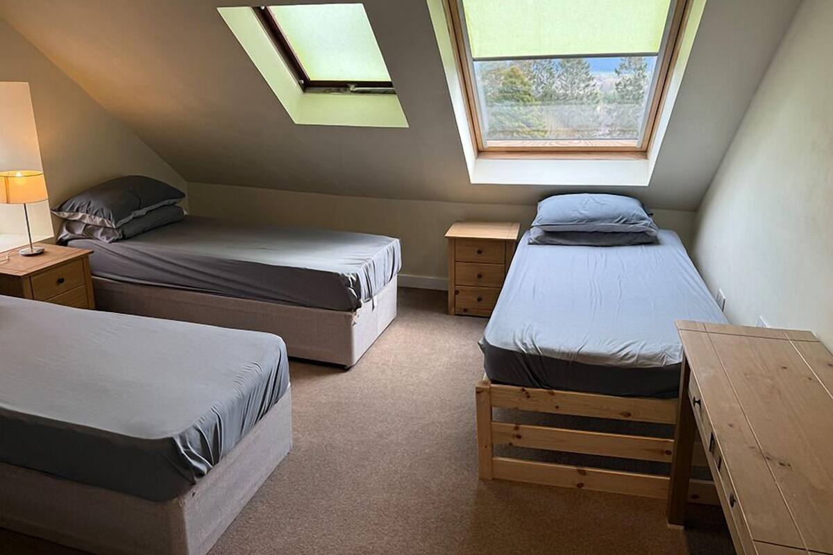 A small, compact room with two beds, a nightstand, a wooden table, and skylights.
