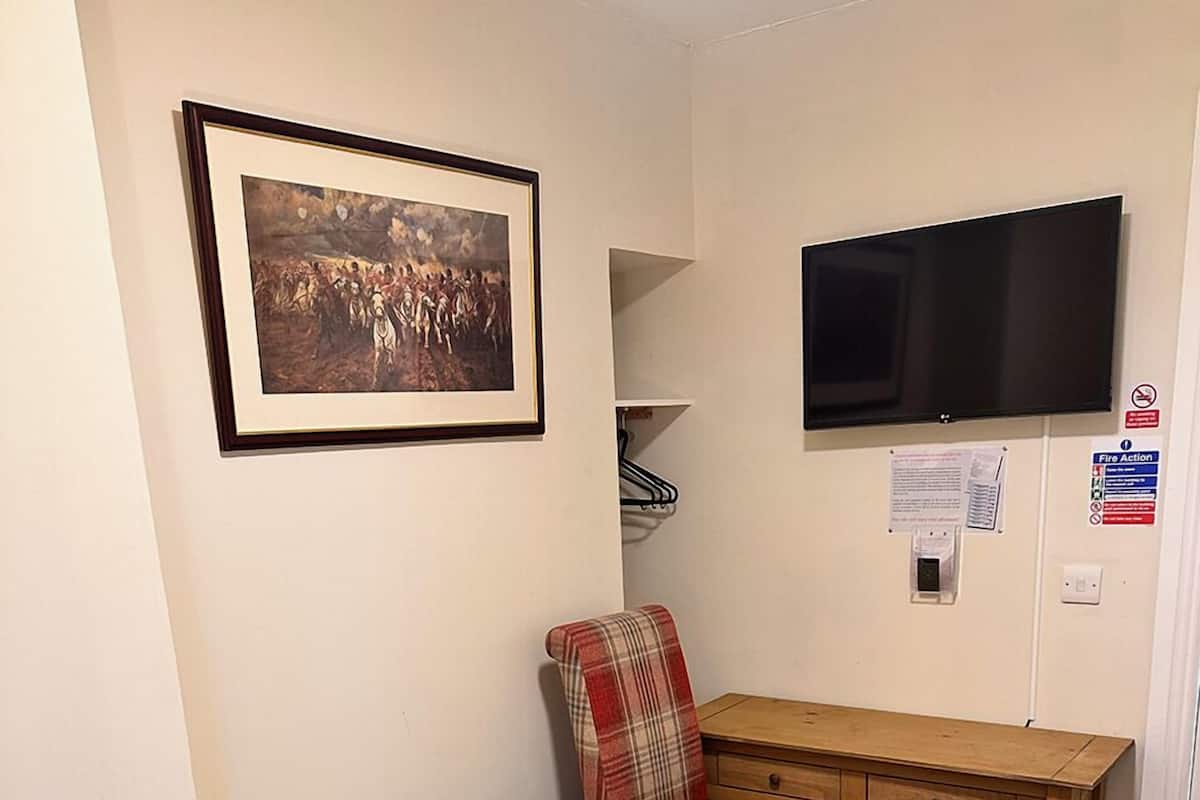 A small, neatly arranged bedroom with a bed, a desk, a chair, a television, and a framed picture on the wall.