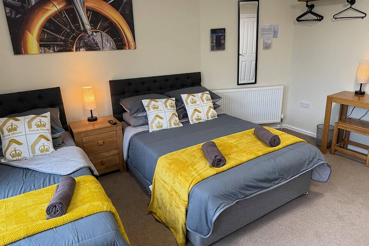 A hotel room with two beds, a nightstand, a mirror, a radiator, and a wooden table with a lamp.