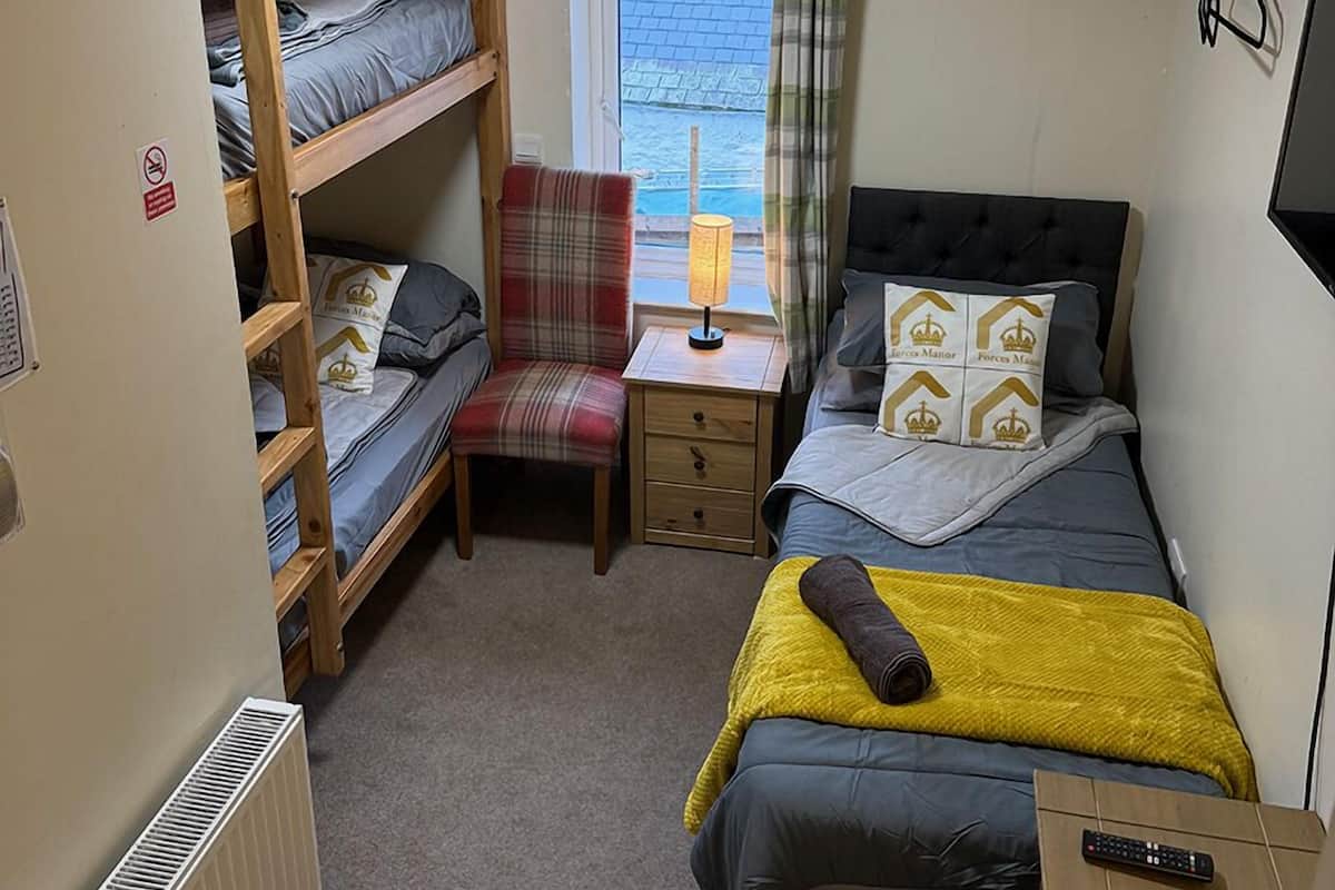 A compact room with bunk beds, a desk, a chair, and a bed.