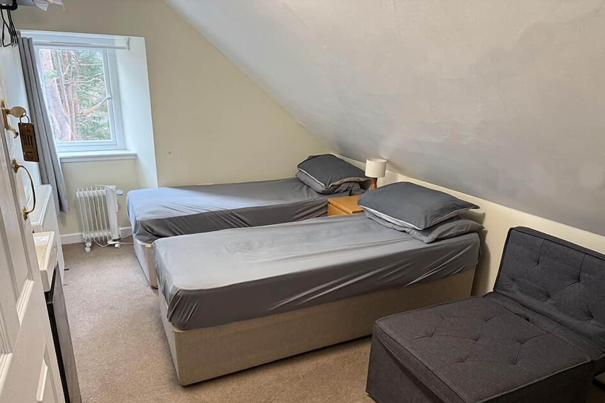 A small, cozy room with two single beds, a small table, and a chair.