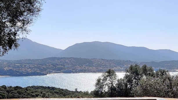 A wooden deck with a pool and lounge chairs overlooking a scenic view of a lake and mountains. - Résidence Licciola (Olmeto)