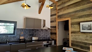 A modern kitchen with a dark countertop, hexagonal tiles, and wooden beams. - Résidence Licciola (Olmeto)