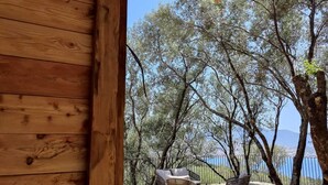 A wooden pergola with a tiled roof overlooking a deck with wicker furniture and a view of trees and a body of water. - Résidence Licciola (Olmeto)