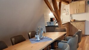 Un comedor con mesa de madera y sillas grises, una cocina al fondo y vigas de madera en el techo.