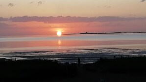 Una puesta de sol sobre un mar tranquilo, con la silueta de una persona de pie en la orilla.