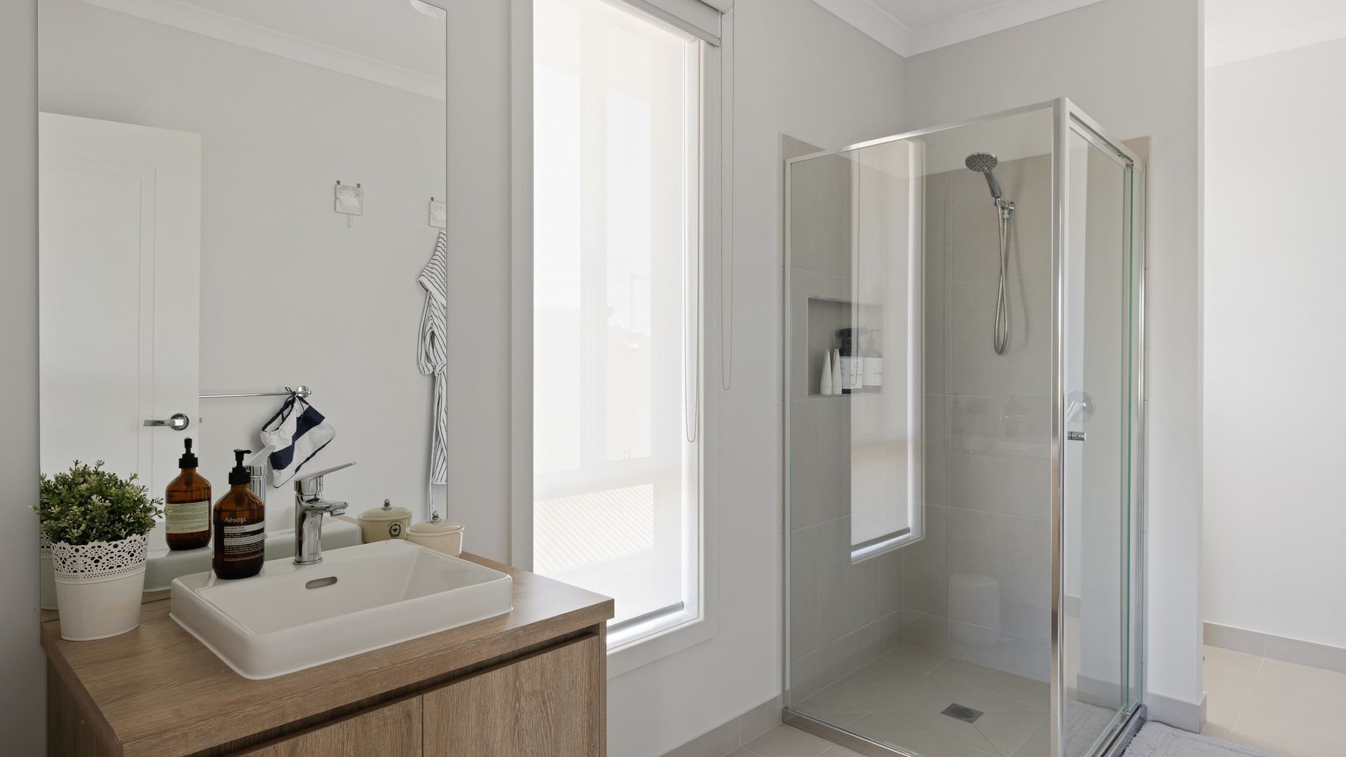 A modern bathroom with a large sink, a glass shower enclosure, and a window providing natural light.