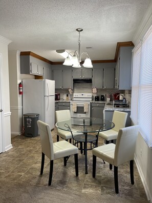 Compact kitchen area with a round dining table and four chairs, featuring a refrigerator, stove, and microwave.