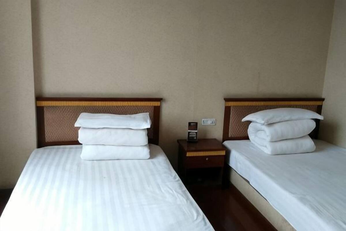 Two single beds with wooden headboards, white linens, and a nightstand with a clock between them.