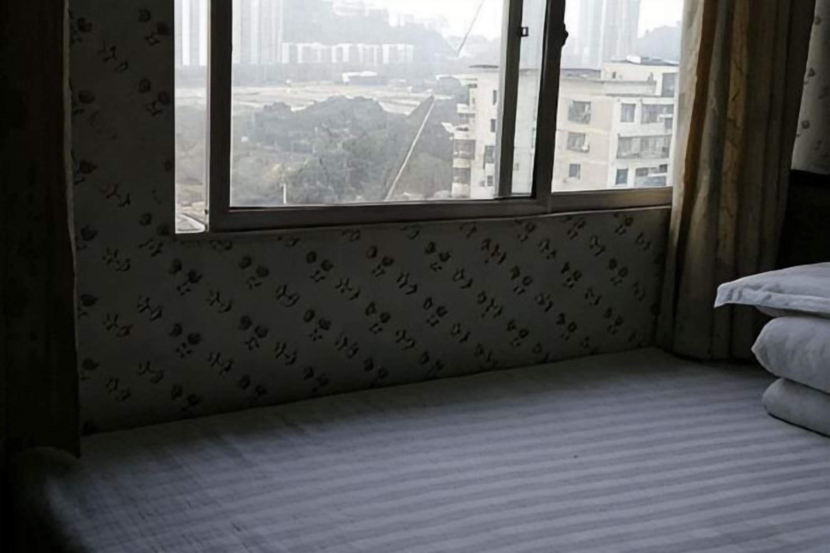 A hotel room with a large window, a bed, and a patterned wall.