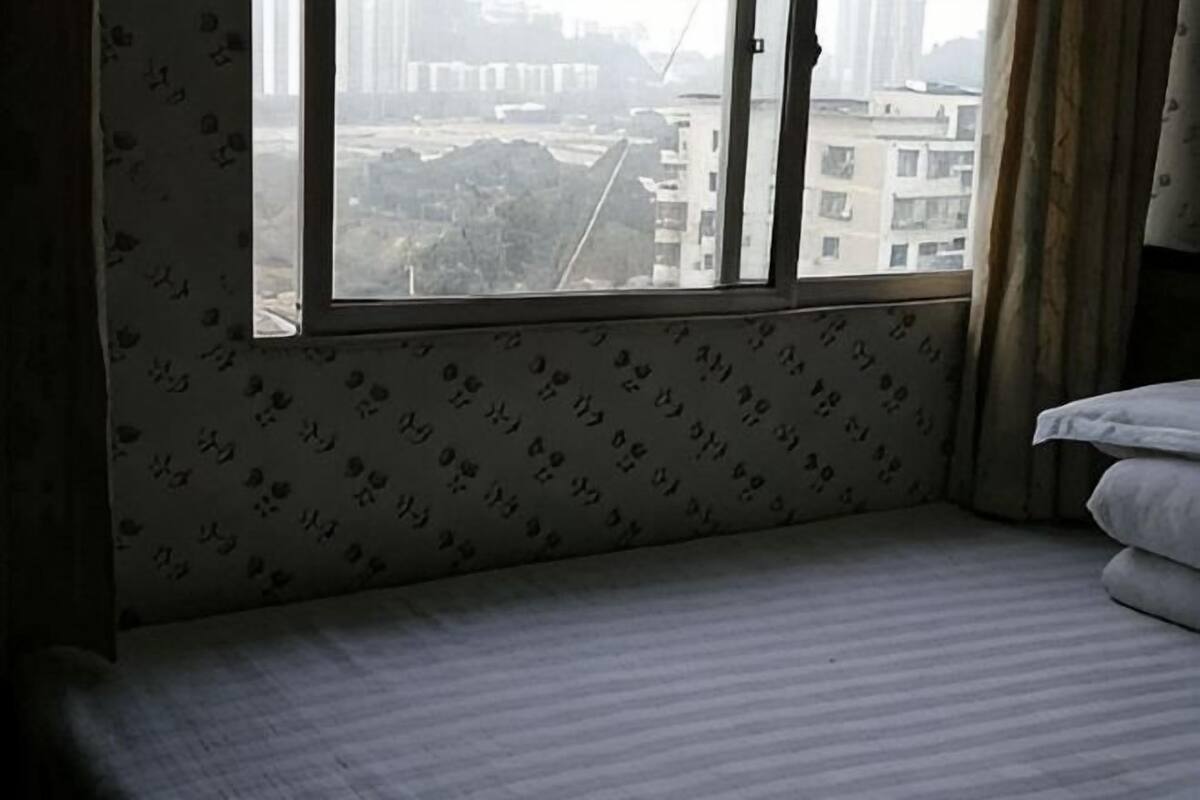 A hotel room with a large window, a bed, and a patterned wall.