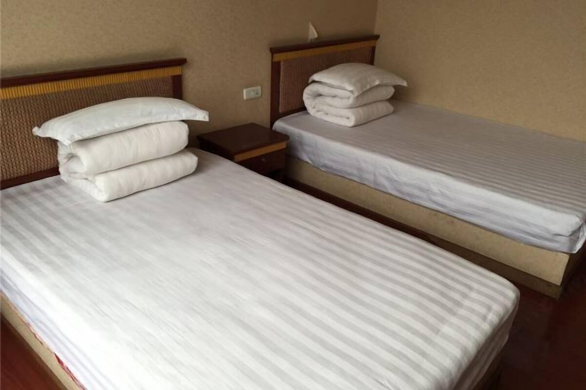Two single beds with white linens, wooden headboards, and a small wooden nightstand with a lamp between them.