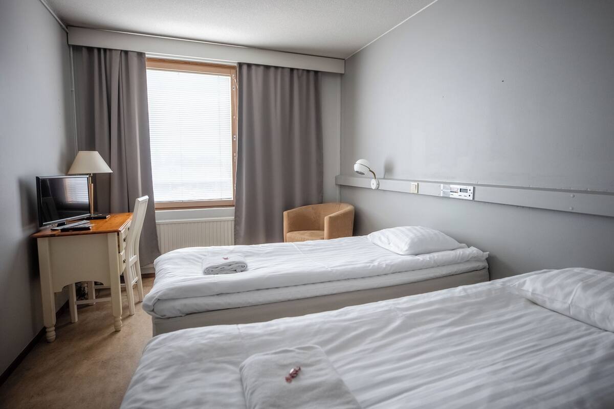 Une chambre d’hôtel avec deux lits, un bureau avec une lampe, une chaise et un téléviseur.