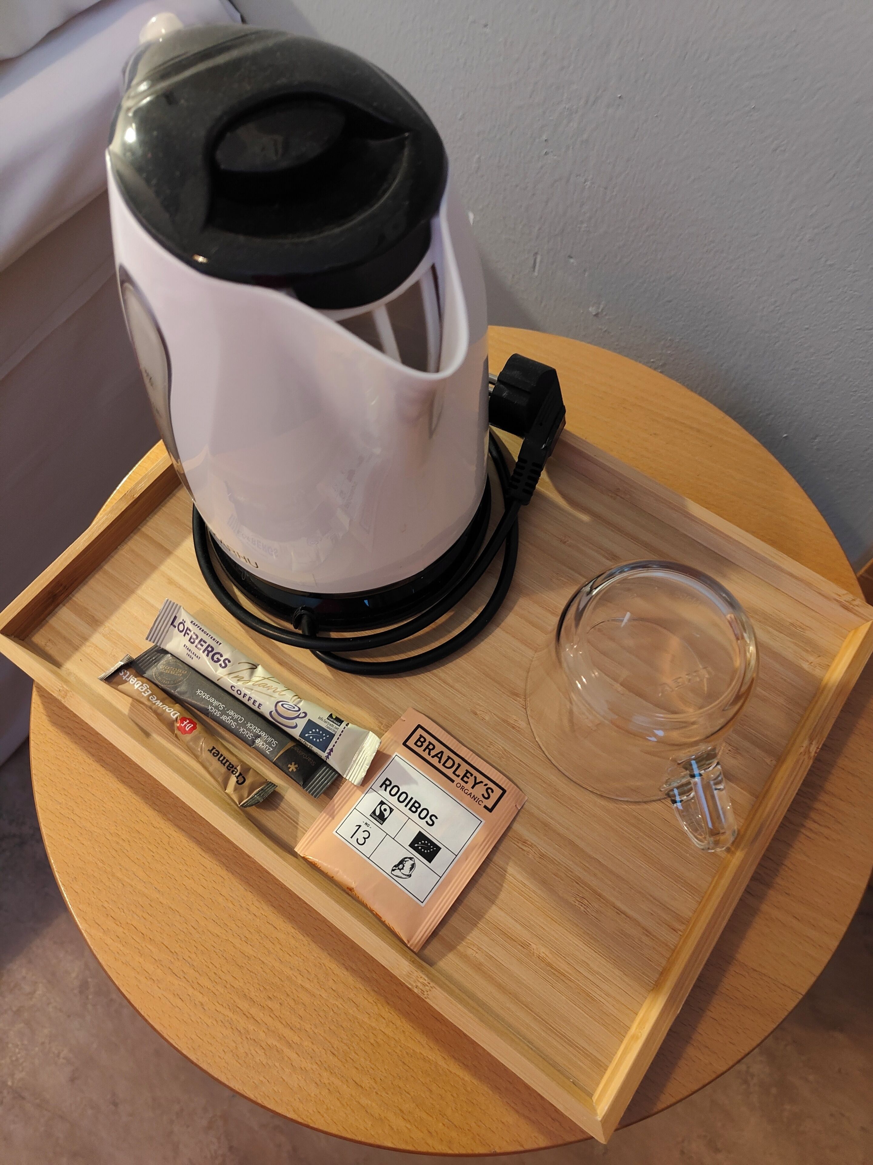 A coffee maker on a wooden tray with coffee pods and a glass.
