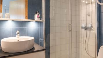 A bathroom with a white sink, a mirror, a shower enclosure, and a toilet.