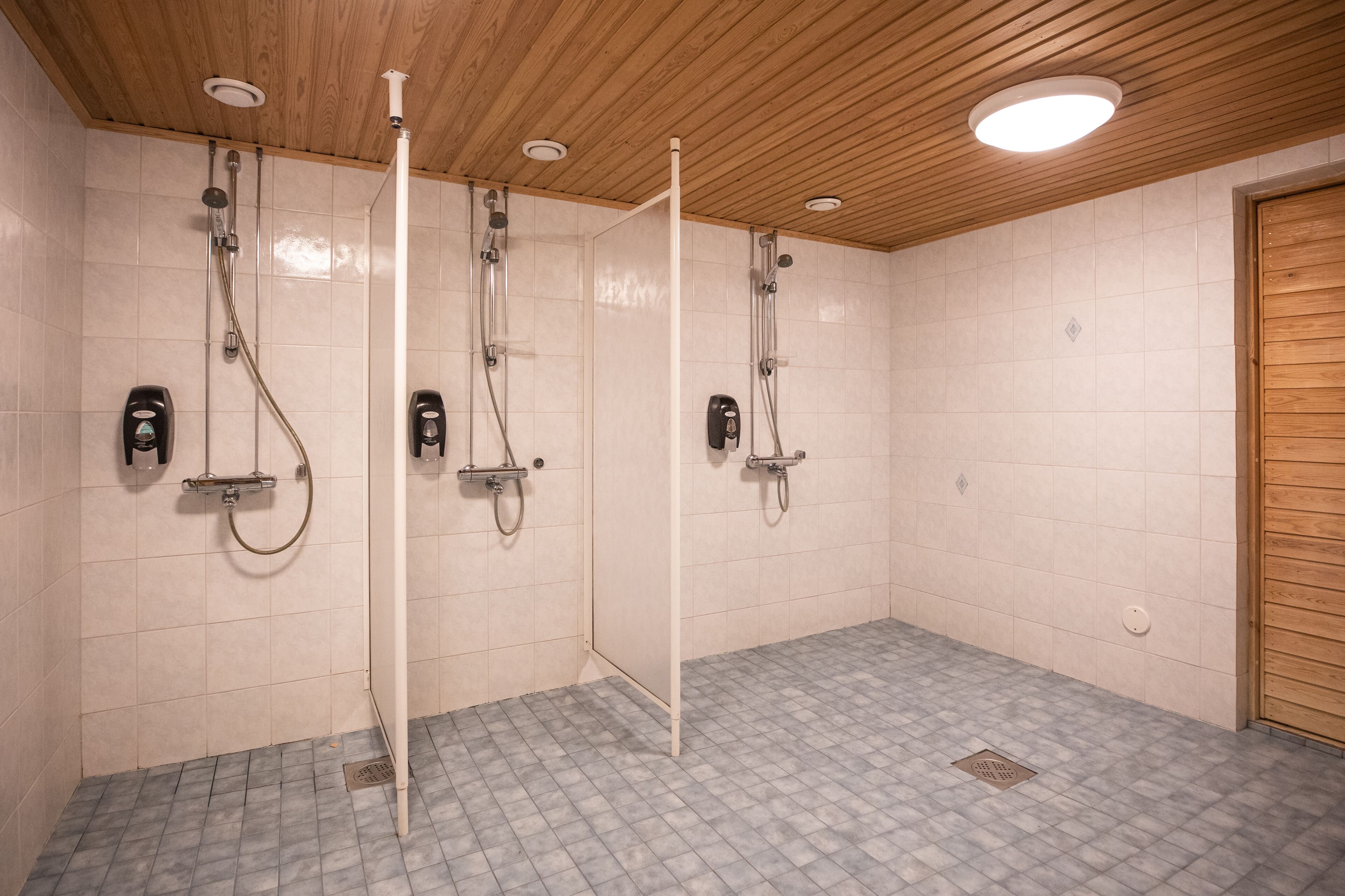 Un área de ducha con tres cabezales, techo de madera y paredes con azulejos.