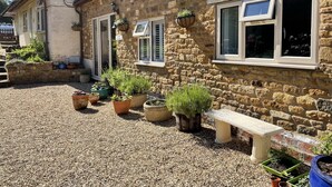 Un bâtiment en pierre avec une cour recouverte de gravier, des plantes en pot et un banc.