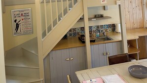 A multi-level interior with a staircase, a dining area with a table and chairs, and a kitchen area with cabinets and a sink.