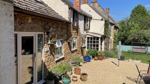 Une maison traditionnelle en pierre, dotée d’une cour en gravier, de plantes en pot et d’une enseigne indiquant l’entrée réservée aux invités.