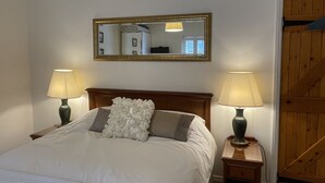 A neatly made bed with a white comforter and decorative pillows, flanked by two bedside lamps on wooden nightstands. A large mirror hangs above the bed, reflecting part of the room.