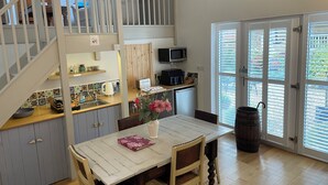 Une cuisine avec une table en bois, des chaises, un four à micro-ondes et un évier. Un escalier mène à une mezzanine.