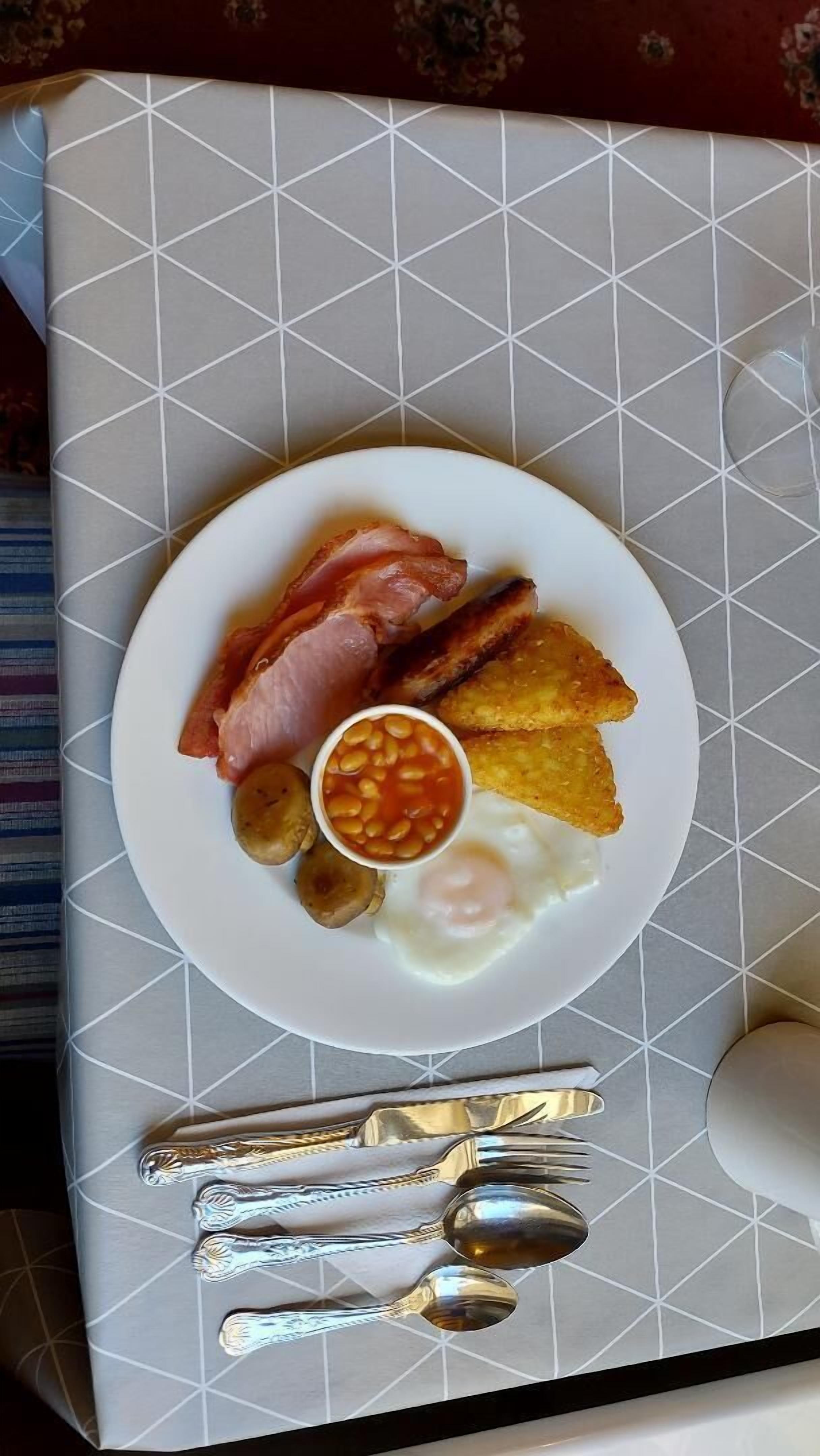 A plate of breakfast food including bacon, eggs, beans, and toast on a table with a geometric patterned tablecloth.