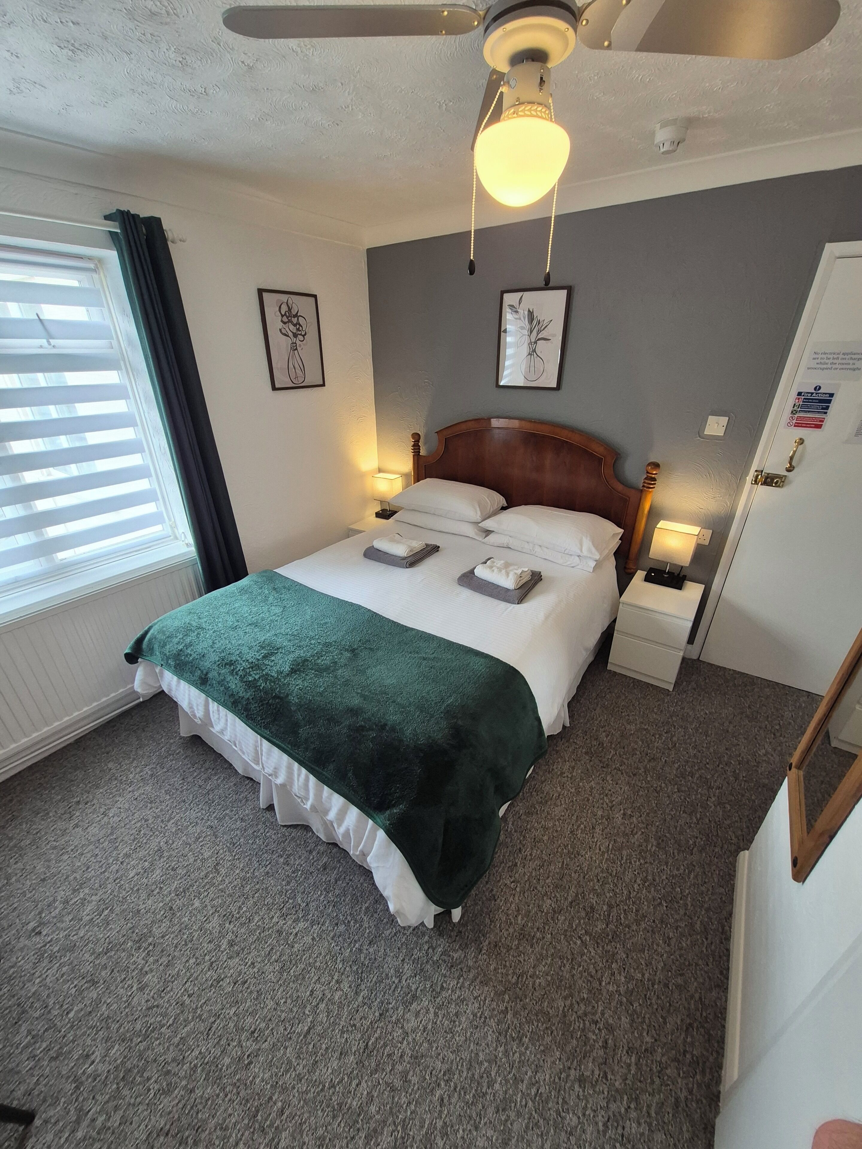 A neatly made bed with a green blanket, a wooden headboard, bedside lamps, and framed artwork on the walls.