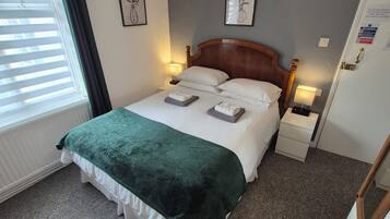 A neatly made bed with a green blanket, a wooden headboard, bedside lamps, and framed artwork on the walls.