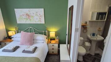 Habitación de hotel con cama, mesitas de noche, un cuadro, un baño con lavabo, inodoro y ducha.