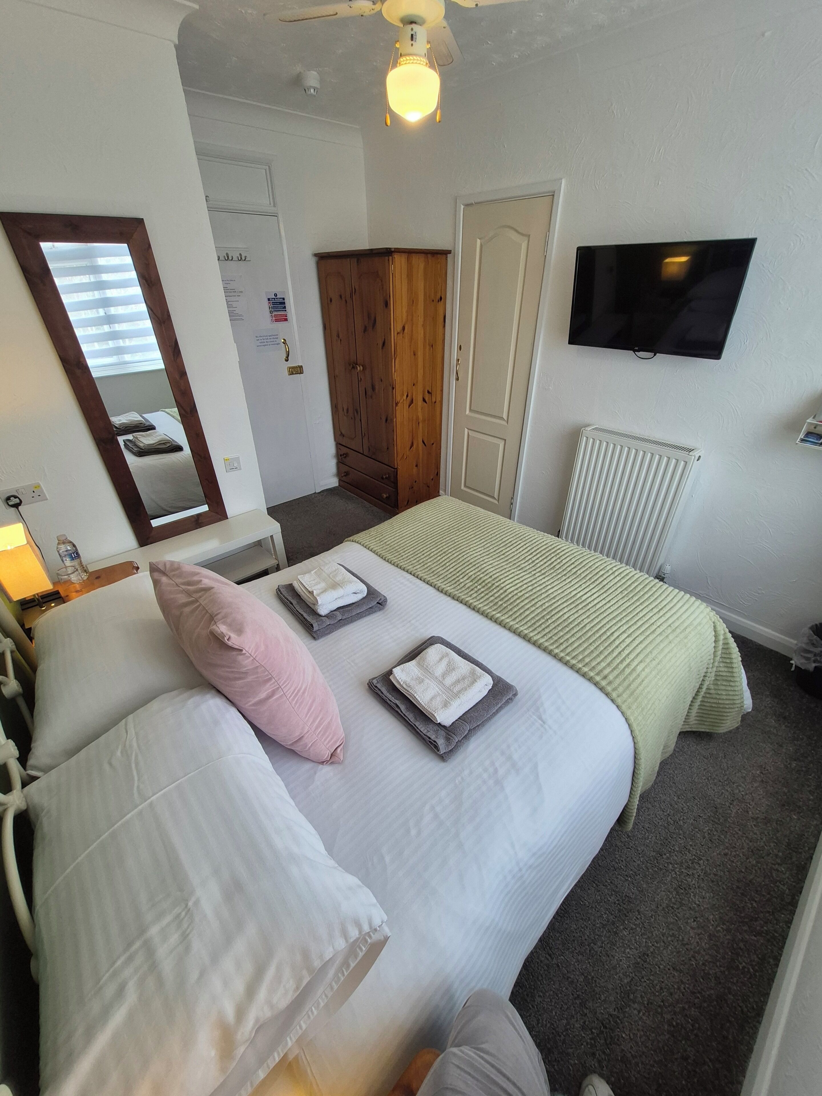 A hotel room with a bed, a television, a wardrobe, and a radiator.