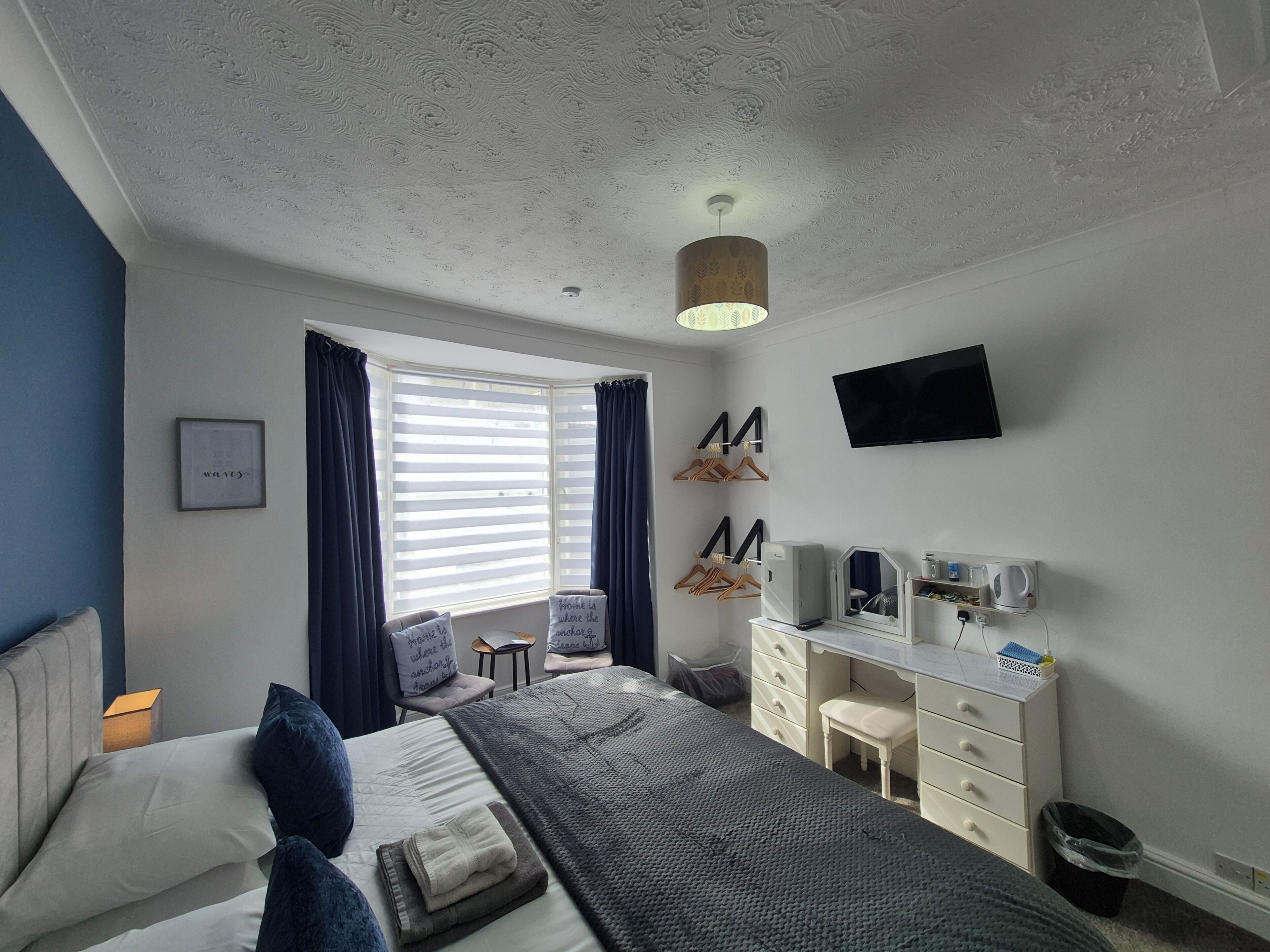 A bedroom with a bed, a desk, a chair, a TV, and a window with curtains.