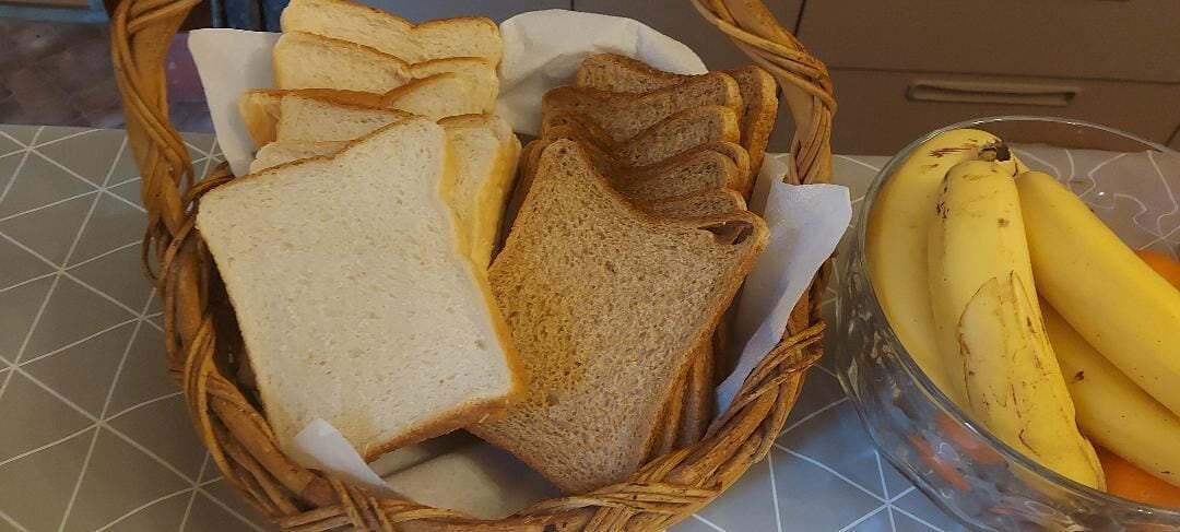 A basket containing slices of white and whole grain bread, and a bowl of bananas.