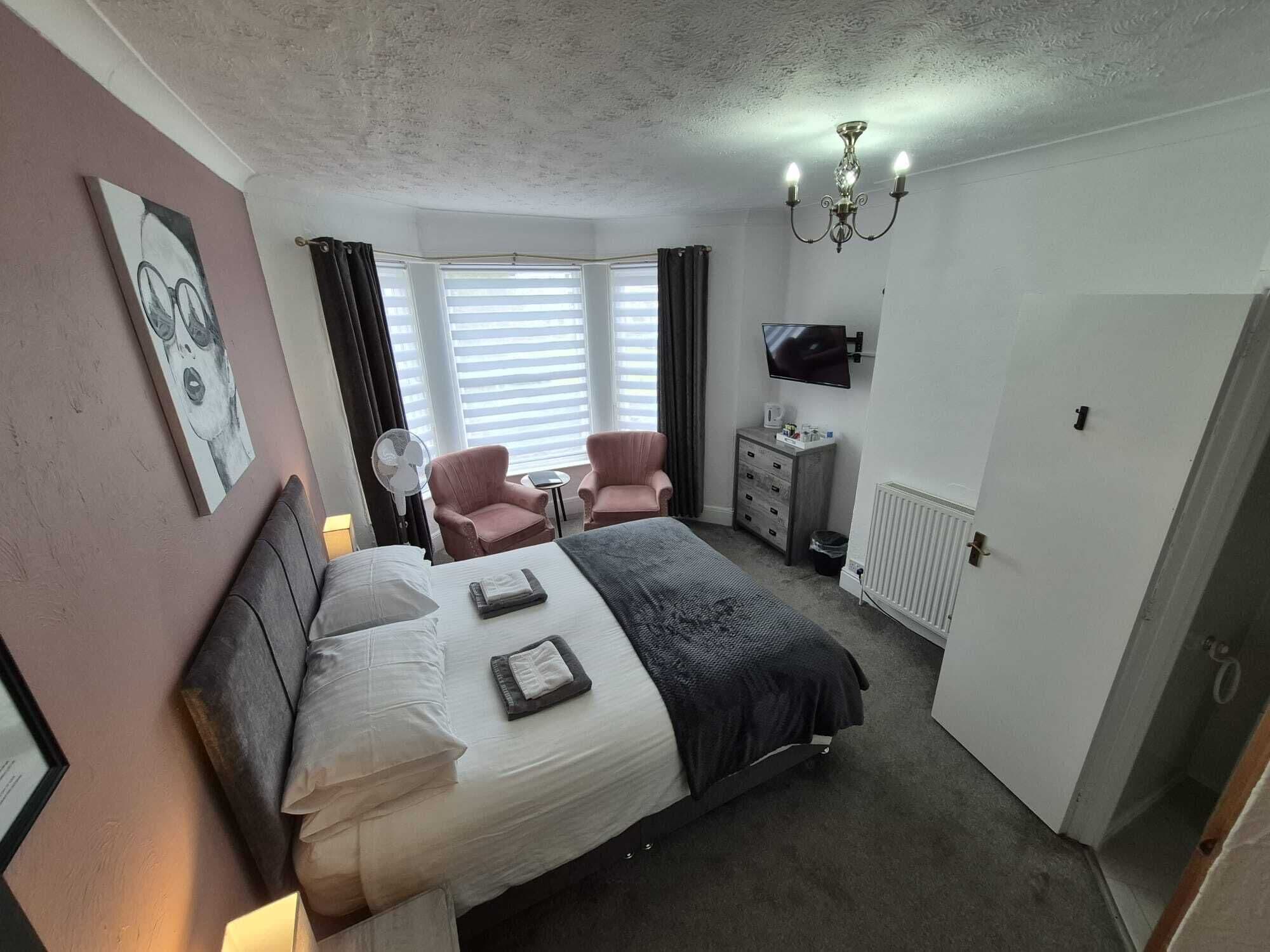 A bedroom with a bed, two chairs, a TV, and a chandelier.