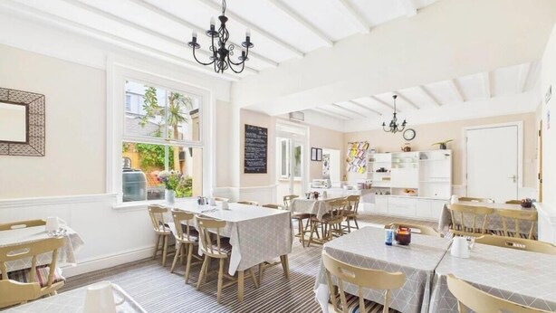 A bright dining area with multiple tables and chairs, large windows, and a view of the outdoors. - The Clifton at Paignton (Paignton)