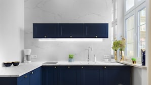 Una cocina moderna con armarios azul oscuro, una encimera blanca y una ventana con plantas.