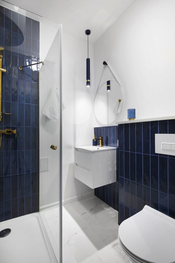 A modern bathroom with a glass shower enclosure, a white toilet, and a sink with a blue-tiled backsplash.