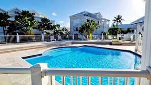A swimming pool with a white fence, palm trees, and a building in the background. - Beachfront the dream holiday (saint martin)