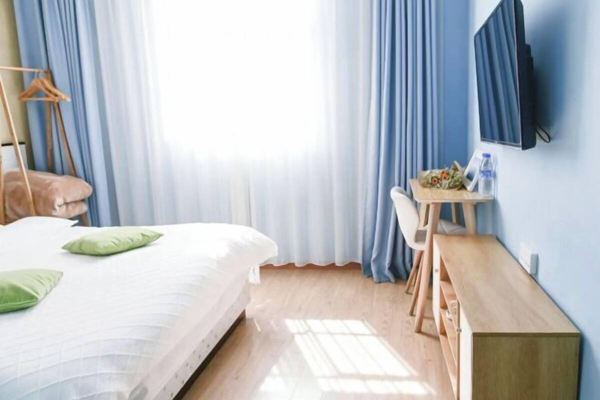 A hotel room with a bed, a desk, a chair, and a TV on the wall.