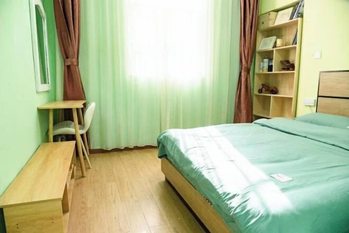 A room with a bed, a desk, a chair, and a shelf with books and toys.