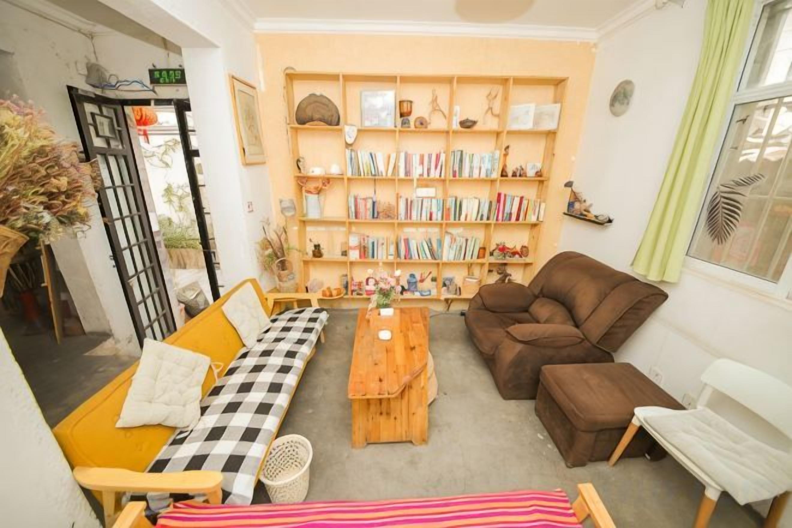 A cozy living room with a checkered sofa, a brown sofa, a wooden coffee table, and a bookshelf filled with books and decorative items.