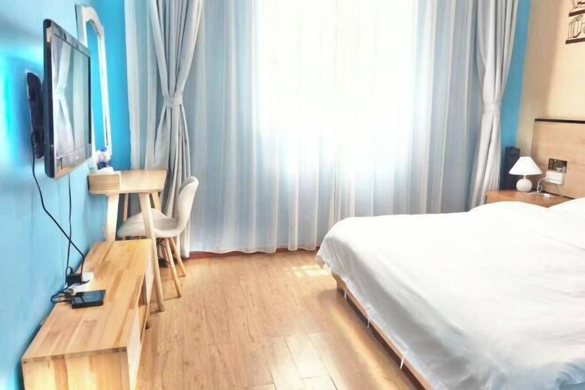 A hotel room with a bed, a desk with a chair, a TV, and curtains.