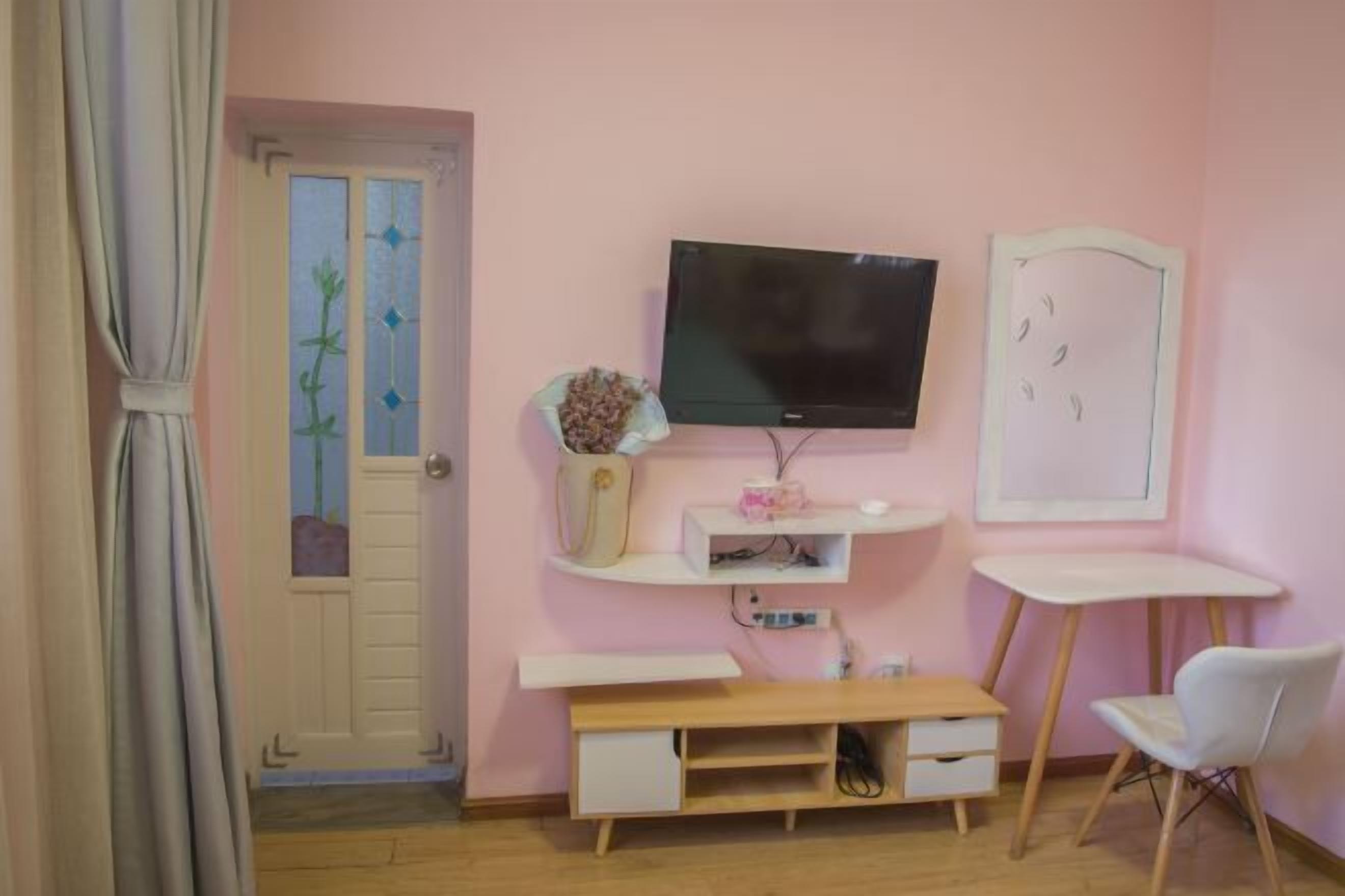 A room with a TV mounted on the wall, a white desk, a chair, and a wooden cabinet.