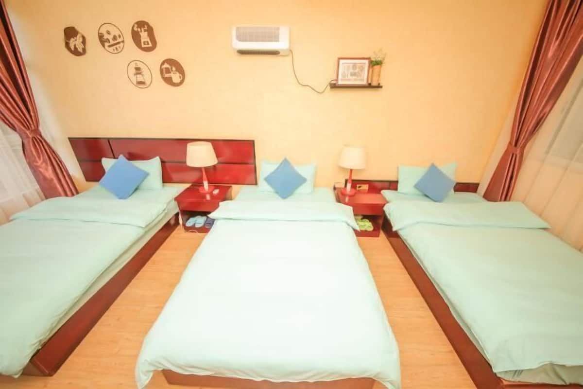 A hotel room with two beds, each with a red nightstand and a lamp. There is a wall-mounted air conditioner and a framed picture above the beds.