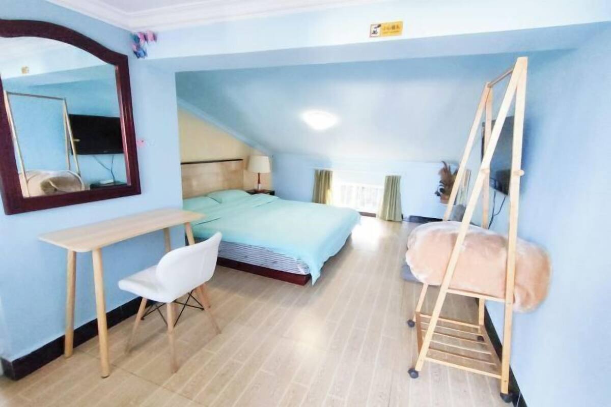 A bedroom with a bed, a desk, a chair, a mirror, and a ladder.