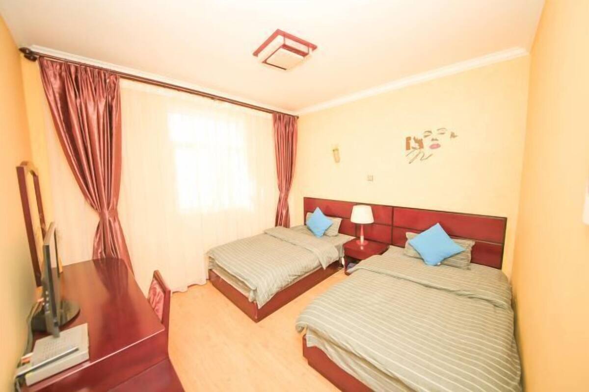 A hotel room with two beds, a desk, a computer, and a window with curtains.