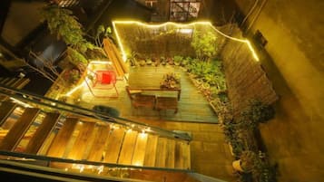 A rooftop garden with a wooden deck, seating area, and string lights.